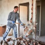 Operaio che demolisce una parete interna durante lavori di ristrutturazione a Napoli, fase di demolizione per redistribuzione degli spazi.